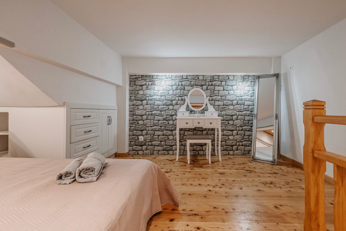 The loft: double bed on pine boards, a dressing table against the stone wall and a full-length mirror.